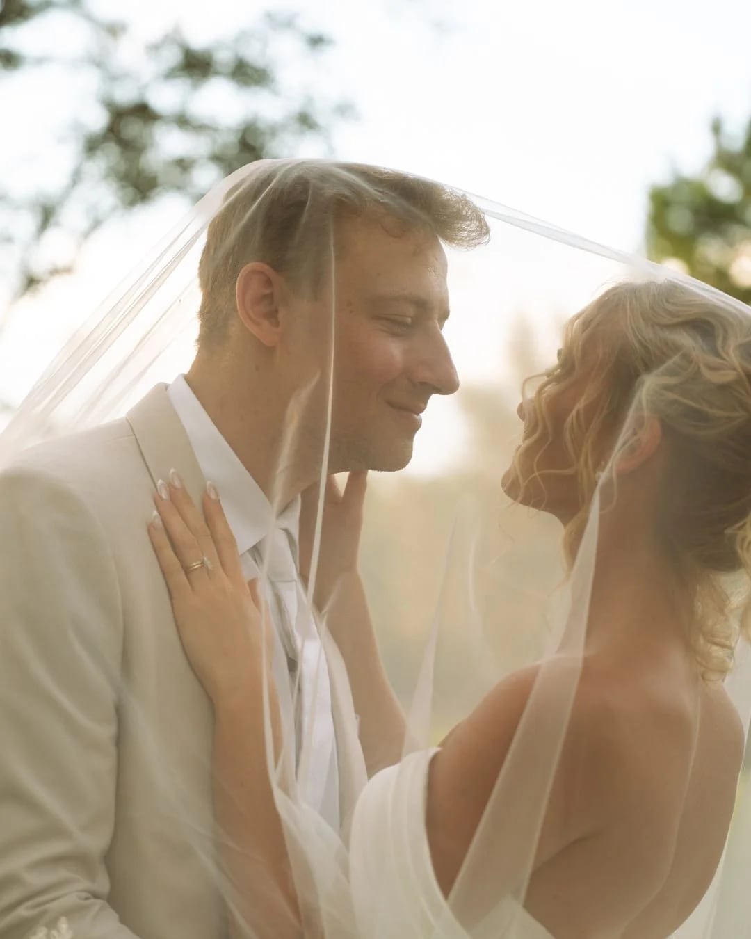 Bride and groom under a wedding veil smiling at each other outdoors