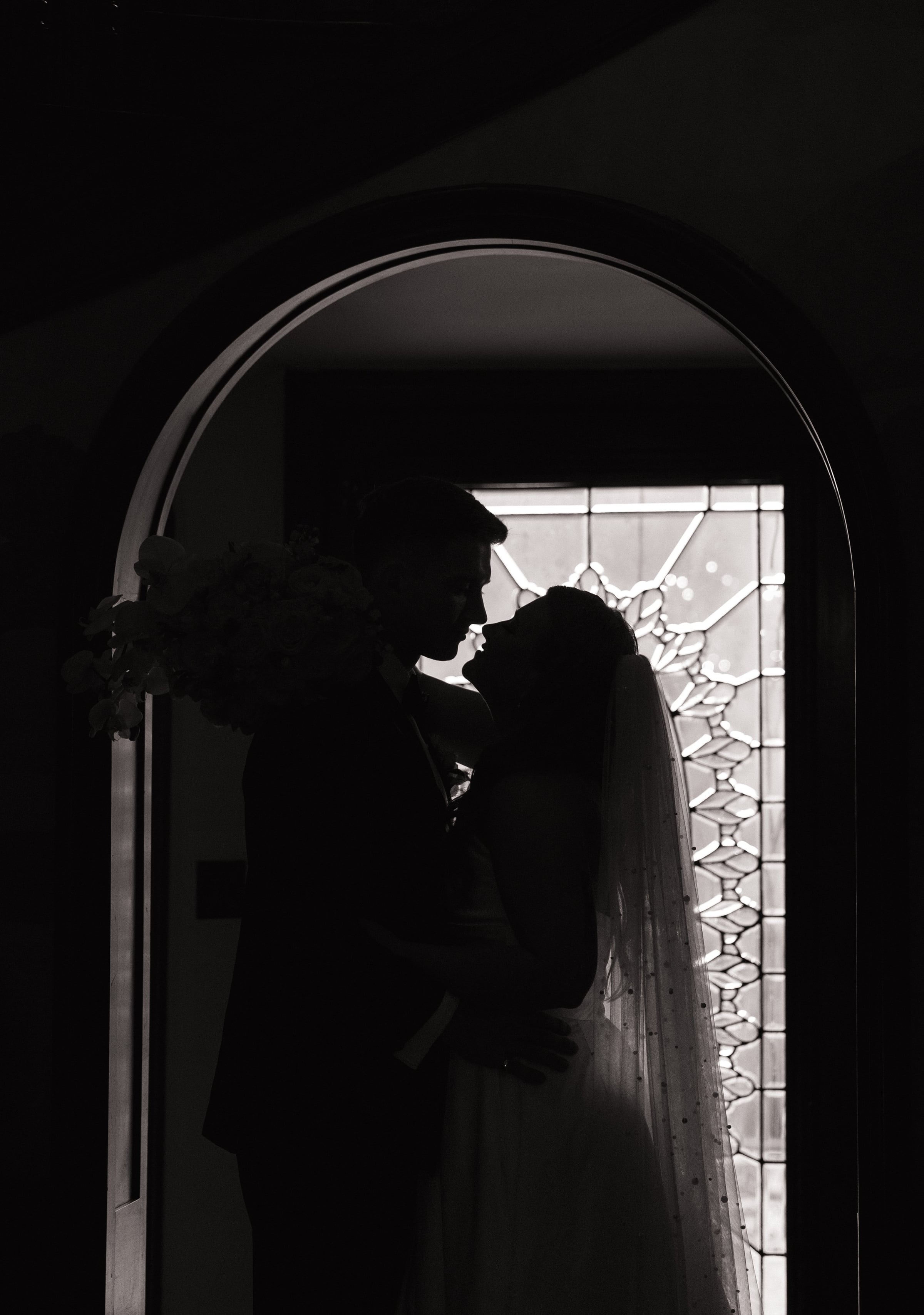 Bride and groom in silhouette before a stained glass window during their wedding