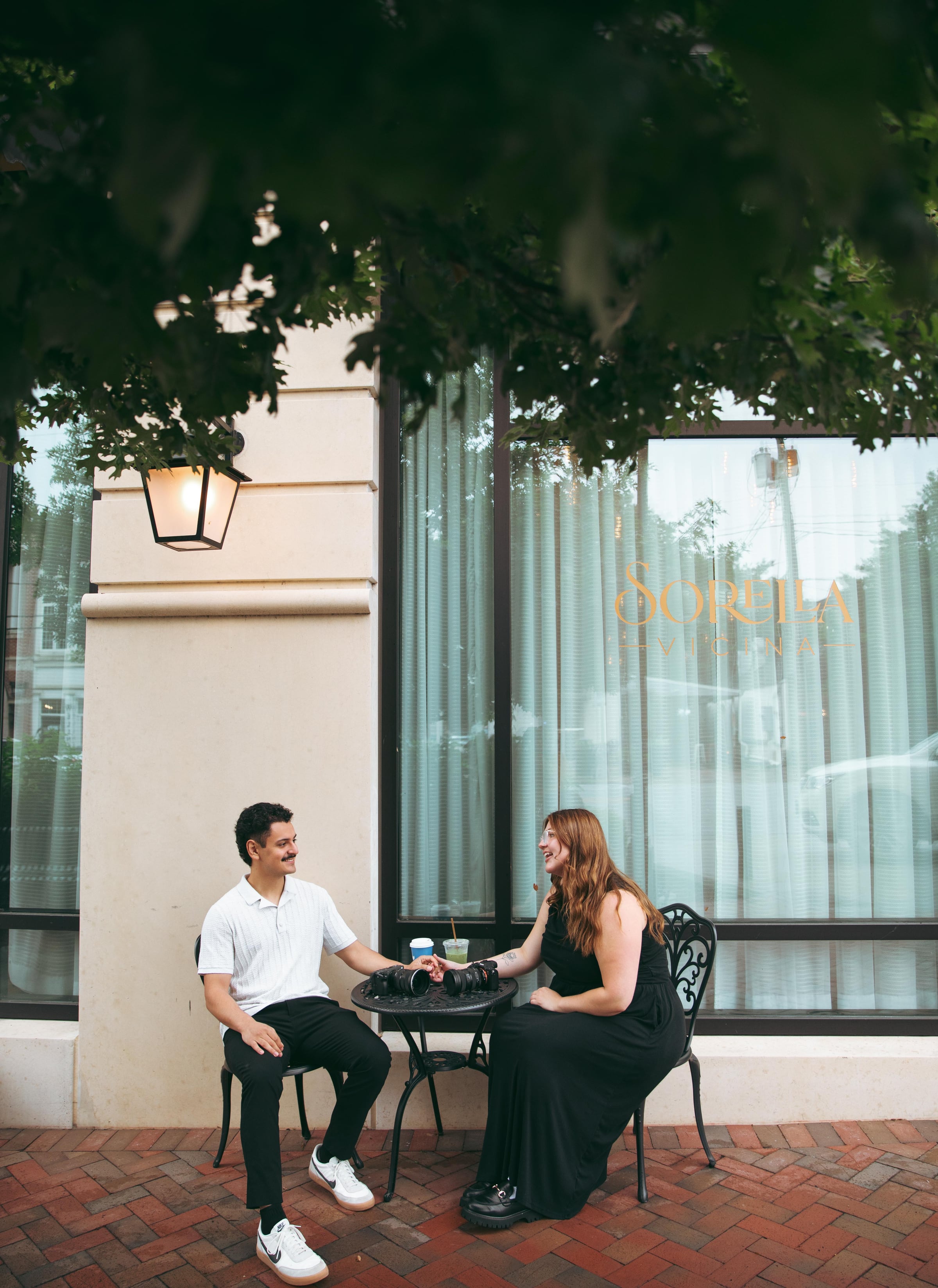 Jo and Mario holding hands at a cafe table with cameras between them