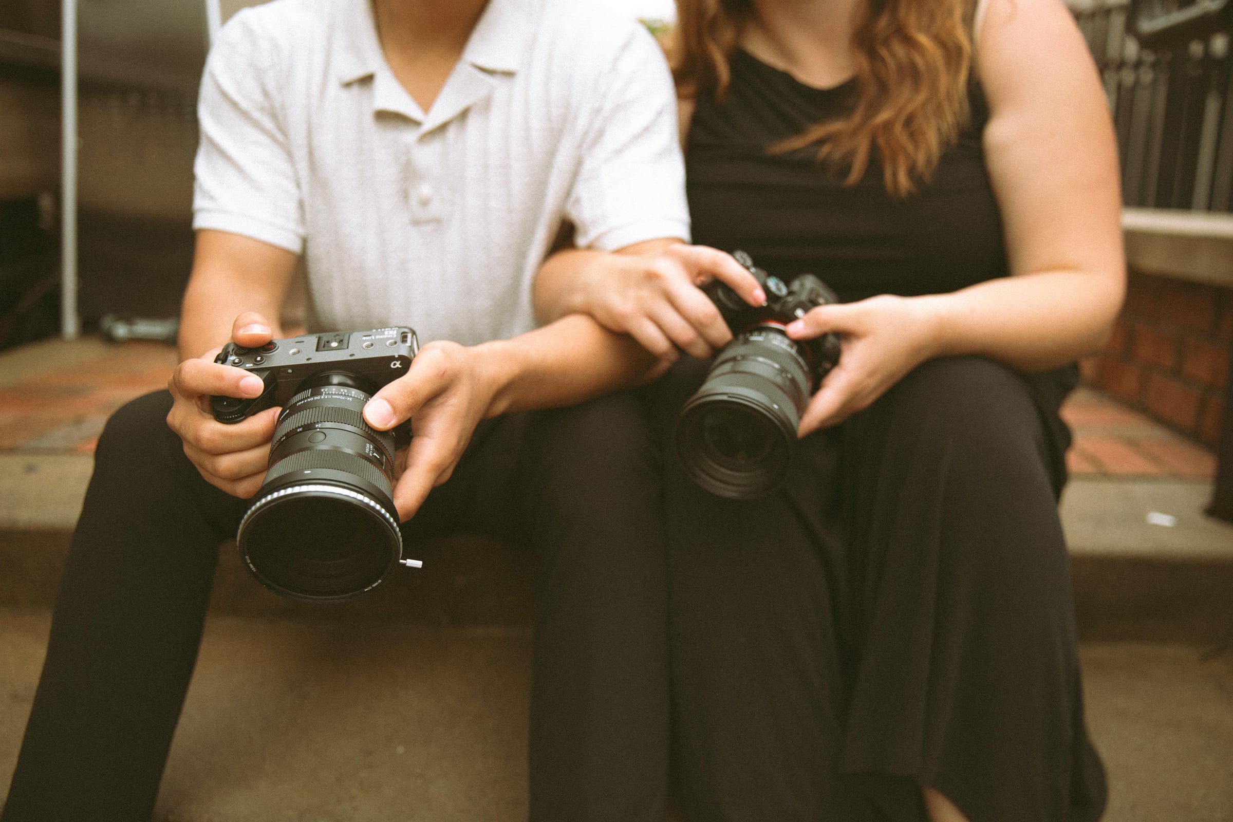 Jo and Mario sitting close, each holding a camera