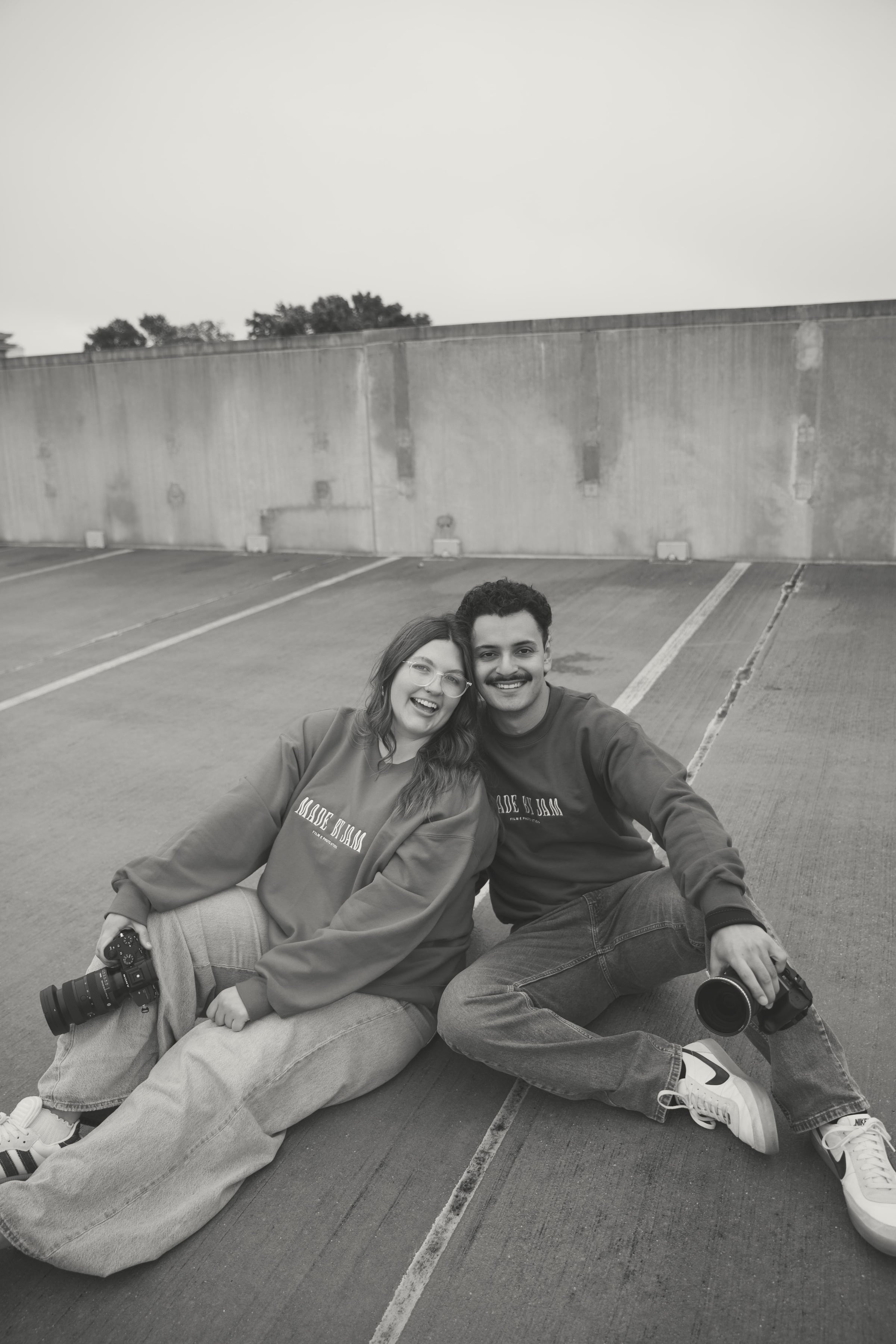 Jo and Mario in black and white, each holding a camera